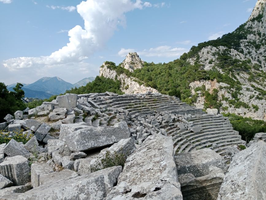 Explore the ancient amphitheater ruins of Termessos, nestled in the mountainous landscape under a clear blue sky.